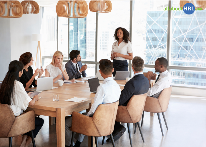Mitarbeitende hören in einer Teambesprechung zu, während eine Person nachdenklich wirkt – eine typische Situation, in der Missverständnisse im Arbeitsalltag entstehen können.